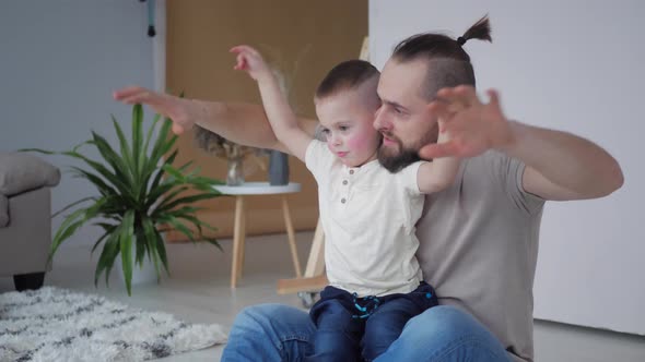 father plays with the boy son in the living room, waves his hands, as if it were the wings of a bird