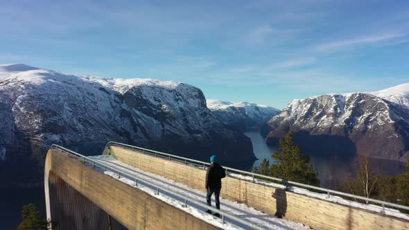 Flying over person walking towards tip of Stegastein viewpoint above Aurlandsfjord - Forwarding aeri alt