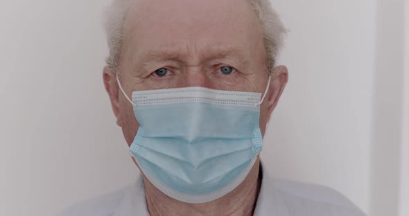 Sad Elderly Man in Medical Mask with Suspected Virus Looking Into Camera alt