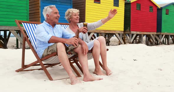 Senior couple toasting drinks near colorful beach hut alt