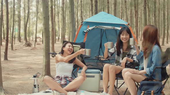 Group of young asia camper friends sitting in chairs by tent in forest alt