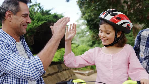 Girl sitting on a bike while happy parents giving high five and hugging her alt