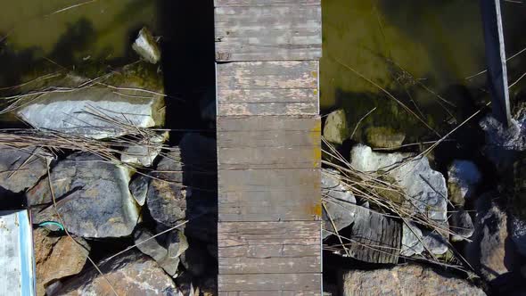 An old pier on a rocky shore with an ancient boat tied to it - straight down bird's eye aerial view alt