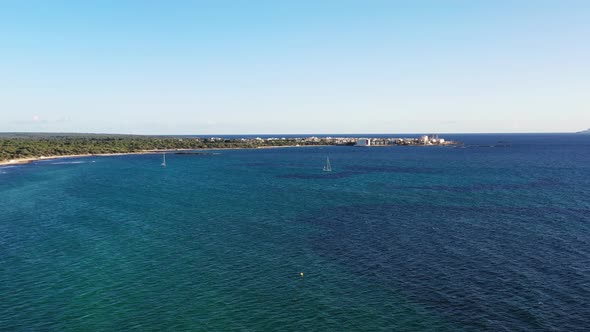 Estanys Beach in Mallorca Island Spain with sailboats near Coto Point hotel resorts, Aerial approach alt
