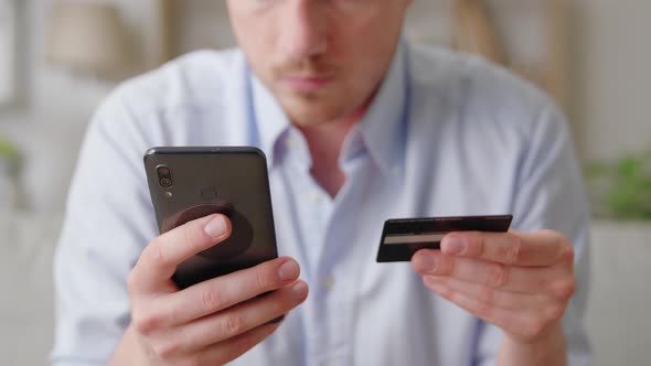 Happy Smiling Young Man Sit on Sofa Buying Online Use Cellphone and Credit Card Close Up alt