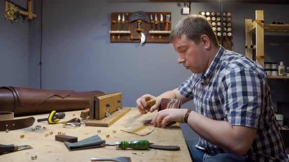 Tailor in a Plaid Shirt Creates a Leather Purse for Individual Design in the Workshop alt