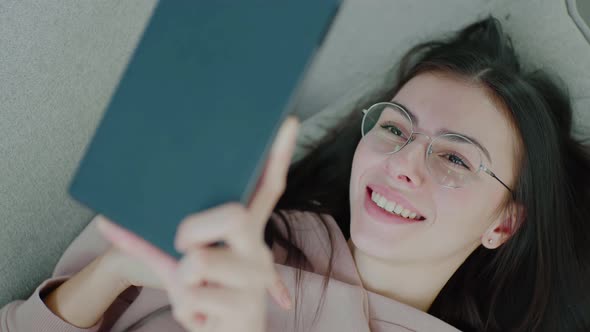 Young caucasian woman with glasses lying on sofa chatting via video call.