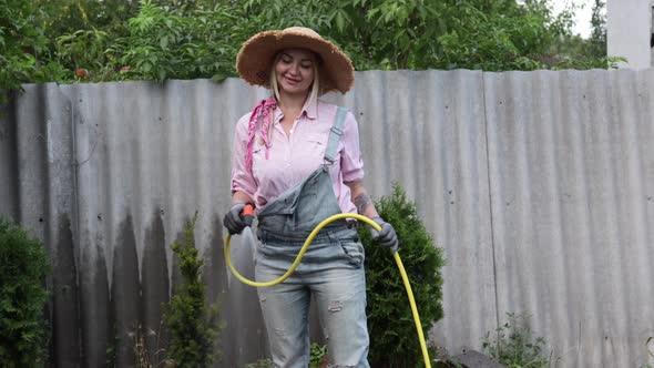 A Young Adult Woman Wateres a Vegetable Garden with a Garden Hose Outside the House alt