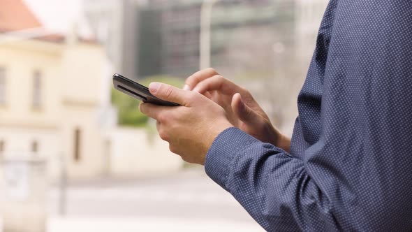 A Man Works on a Smartphone in an Urban Area  Closeup  a Street in the Blurry Background