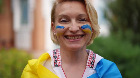 Headshot Portrait of Positive Woman in Embroidered Shirt and Ukrainian Flag Looking at Camera alt