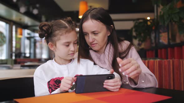 Attractive Caucasian Mother and Her Daughter Using Smartphone at the Cafe