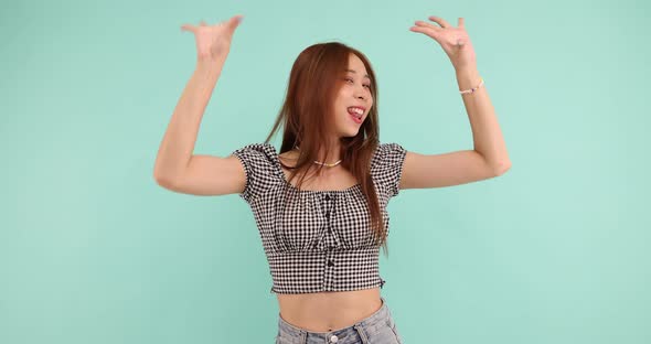 Happy carefree Asian woman dancing and looking at the camera over green background alt