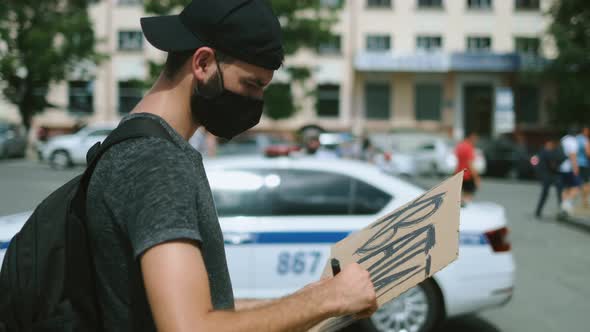 Masked riot activist man drawing poster sign, poster banner. Rebel on rally. alt