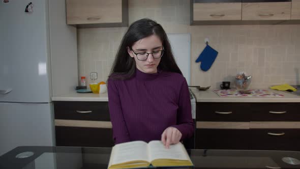 Girl Sitting in the Kitchen in the Evening and Reading Book alt