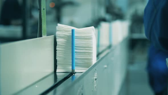 Stack of Paper Napkins Being Placed Onto a Conveyor By a Factory Worker alt