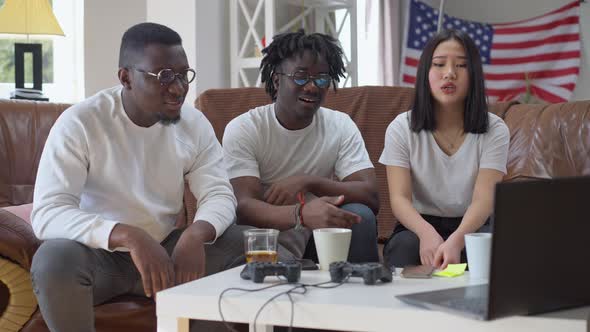 Absorbed Multiethnic Friends Watching Match on Laptop Making Disappointed Facial Expression Talking alt