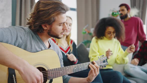 Caucasian Guy Playing Acoustic Guitar in the Company of Mixed Race Friends of Students alt