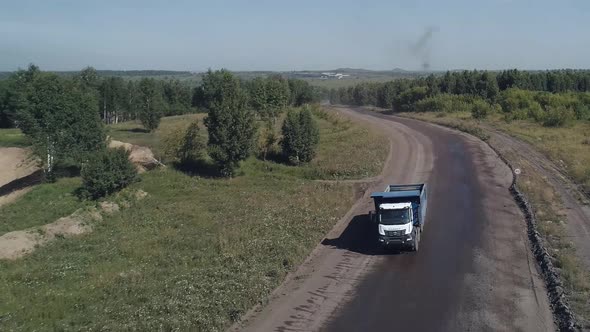 The Drone Flies Up to a Dirt Road Along Which a Heavy Dump Truck is Driving on a Fiveaxle Chassis