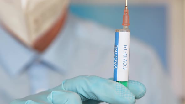 Close up of a researcher with face mask holding a syringe with coronavirus vaccine