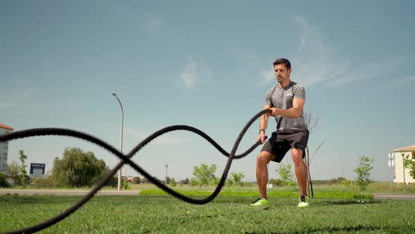 Muscular Caucasian Athlete Makes Waves with a Battle Rope on the Grass Outside