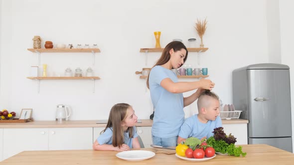 Young Mother Braids Her Son's Hair While Sitting in the Kitchen alt