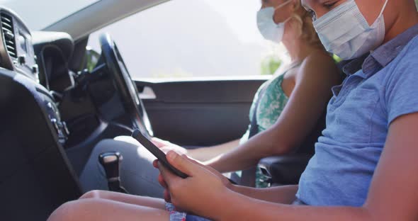 Cauciasian mother and son sitting in car, wearing face masks alt