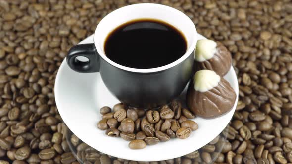 Chocolate Candies And A Cup Of Black Coffee On A Background Of Rotating Coffee Beans Top View.