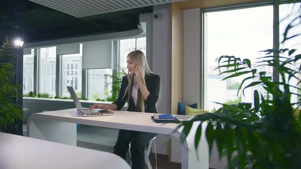 Trendy Business Woman Watching Laptop and Speaking on Phone. Stylish Young Blond Woman Working in alt