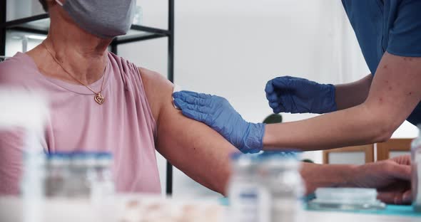 Doctor in Blue Scrubs Medical Gloves Gives Vaccine Injection Shot with Hypodermic Needle to Senior alt