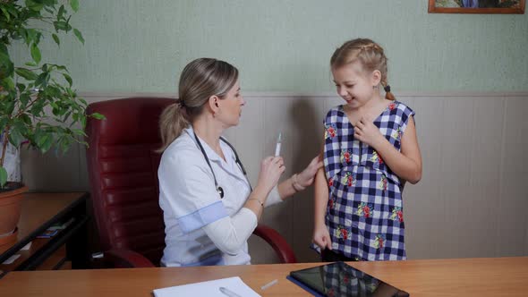 A female doctor in a white coat vaccinates a school-age girl who is very afraid.