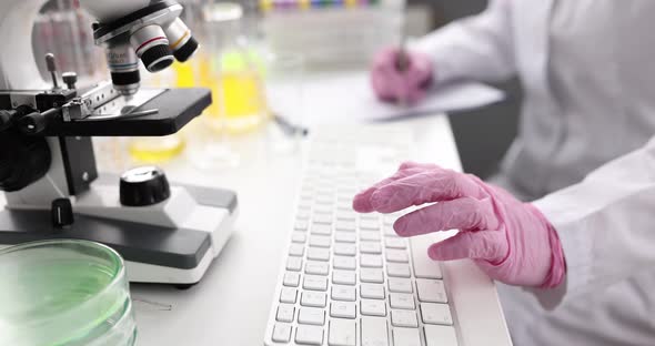 Researcher Works at Table and Types on Keyboard with Microscope