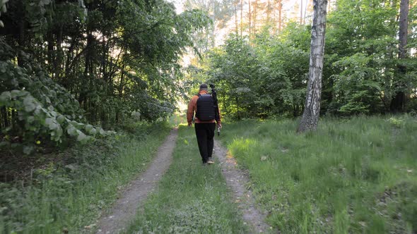 Aerial Drone View Following Young Caucasian Man with Backpack Walking through Forest