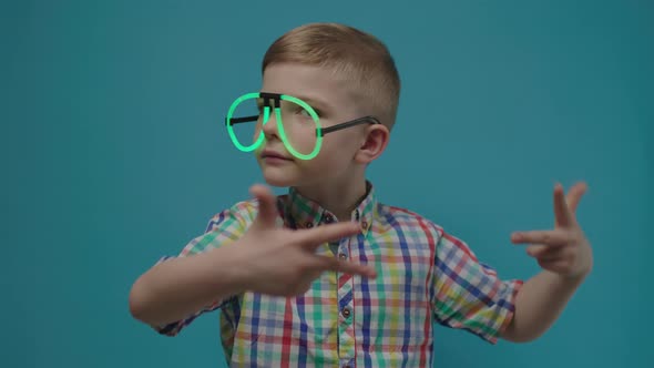 Preschool Boy Wearing Neon Eyeglasses Dancing on Blue Background in Slow Motion alt