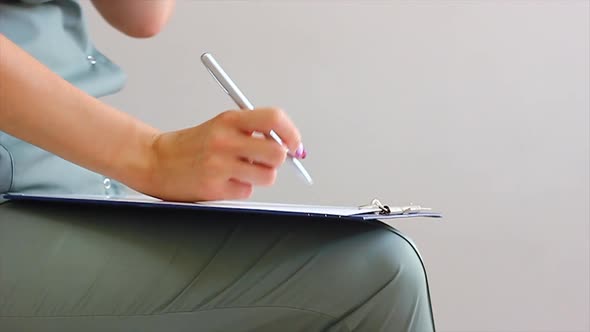 Young Doctor of Caucasian Nationality in a Dark Green Coat Writes with a Pen in a Notebook Closeup alt