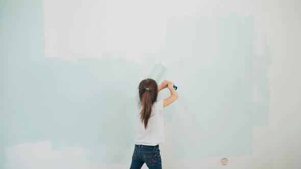 Caucasian Girl Paints a Wall with a Brush A Girl Paints a Wall A Girl Makes Repairs in a Room A Blue alt