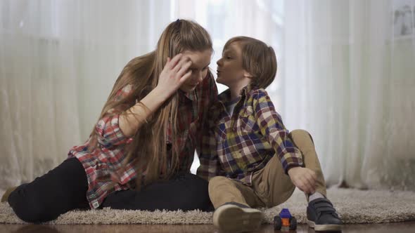 Older Sister and Younger Brother Playing Together Sitting on the Floor on the Fluffy Carpet. The Boy alt
