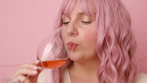 Beautiful 30s Woman with Pink Curly Hair Drinking Rose Wine Over Bright Pink Color Background alt