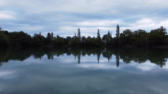 Aerial footage above the lake with reflections of trees and clouds in the water during twilight
