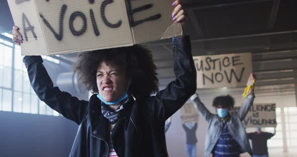 Diverse group of people wearing face masks holding protest signs shouting raising fists alt