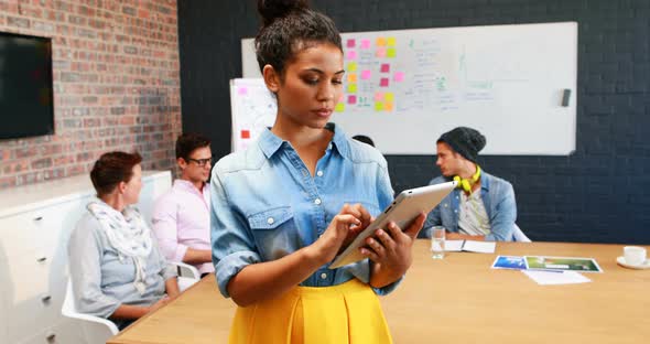 Businesswoman using digital tablet while coworkers interacting with each other alt