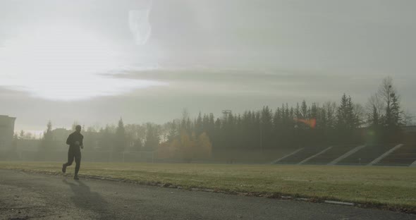 Athlete Is Running at the Stadium in the Morning in the Foggy Autumn Weather  alt