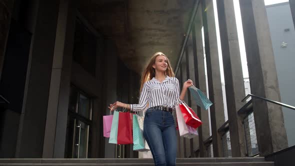 Smiling Girl Walking From Centre Mall with Shopping Bags, Happy with Purchase on Black Friday alt