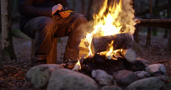 Man Using Compass and Smart Phone By Campfire in the Woods