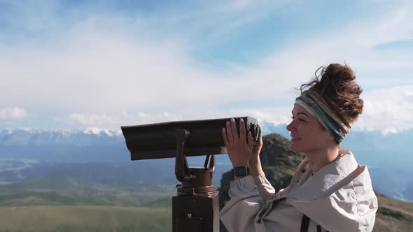 Attractive Girl Tourist on the Observation Deck Looks at the Mountains Through Binoculars