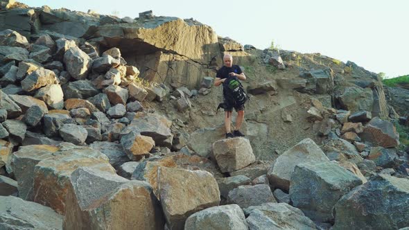 traveler with a backpack in shorts and a black t-shirt is sitting on a large rock alt