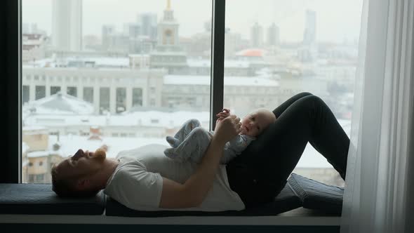 father and little son lie on the window sill with a view of the city