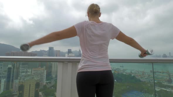 Woman Doing Shoulder Exercises on the Balcony. Hong Kong, China alt