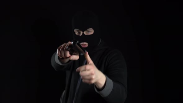 A Man in a Balaclava Mask Stands with a Gun. A Thug Points His Gun at the Camera. On a Black alt