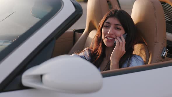 Beautiful Stylish Woman Sits in Her Luxury White Convertible and Talks Via Smartphone with Her