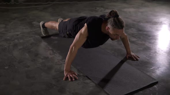 Caucasian Man with Dreadlocks in Black Sportswear Does Pushups in Empty Gym or Studio alt